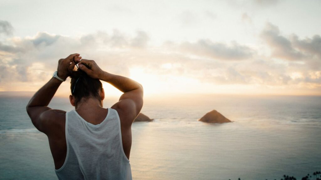 man in a white sleeveless shirt facing the sunset along the coast